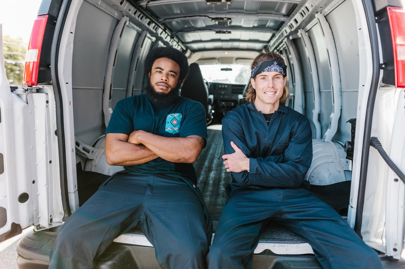 Zwei lächelnde Handwerker sitzen im Laderaum ihres Transporters (Foto: RDNE Stock project / Pexels)