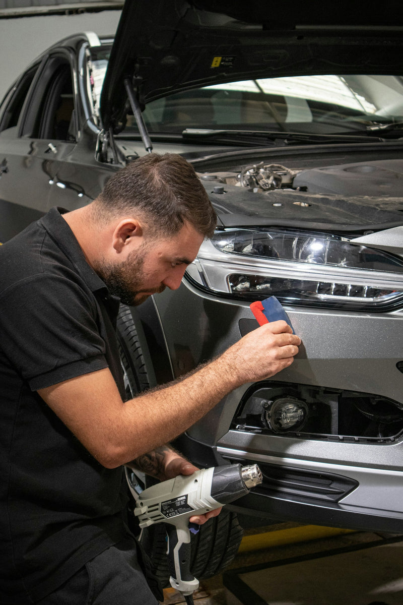 Folienprofi verklebt Folie am Stoßfänger eines Fahrzeugs (Foto: Deniz Demirci, Unsplash)